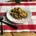A white plate that has cheeseburger macaroni that was made in an Instant Pot on it. The plate is sitting on a red and white placemat. Next to the plate is a fork and knife.
