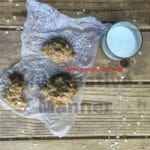 Three peanut butter no bake cookies on wax paper with a glass of milk next to them.