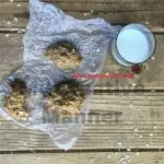 Three peanut butter no bake cookies on wax paper with a glass of milk next to them.