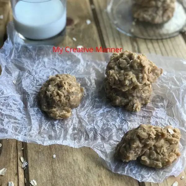 Three peanut butter no bake cookies on wax paper with a glass of milk and a jar with more cookies in it.