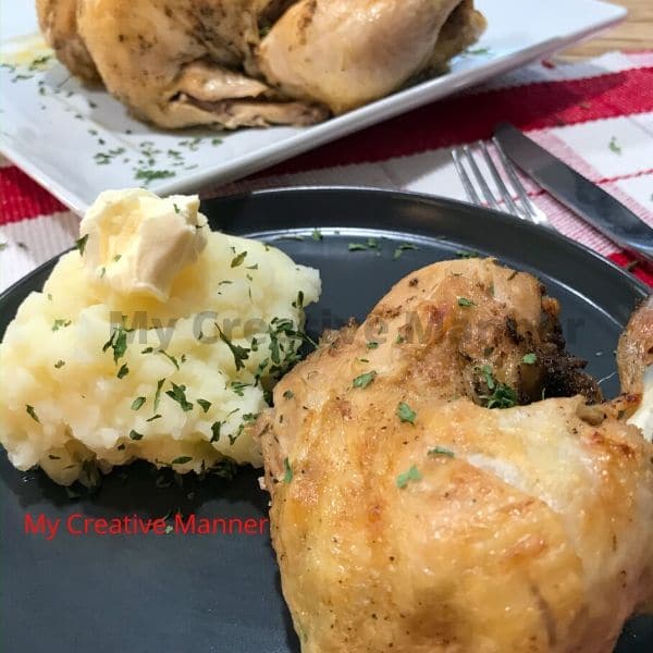 A chicken leg quarter on a plate with mashed potatoes. Behind the plates is another plate with the whole chicken on it that was cooked in an Instant Pot.