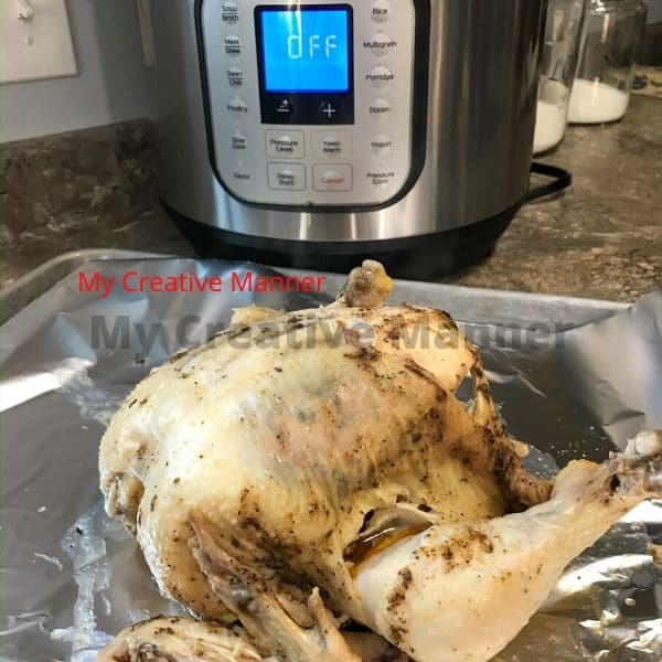 An Instant Pot in the background with a whole chicken on a cookie sheet.