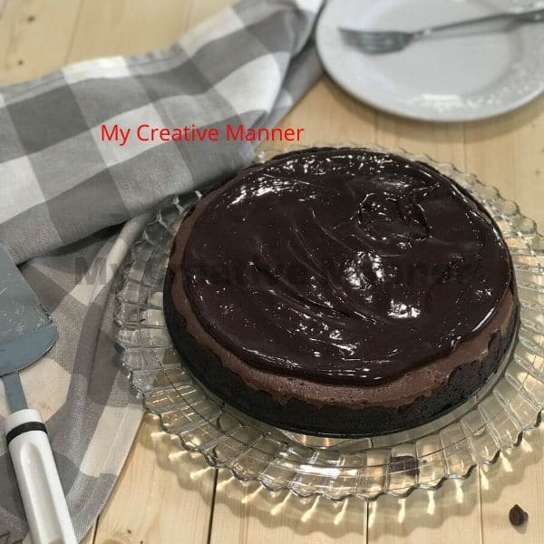 Triple chocolate cheesecake recipe on a glass plate with a white and grey napkin next to it.