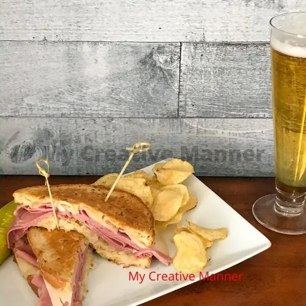 Corned Beef Reuben on a plate with pickle, chips, and a beer.