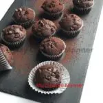 Double chocolate muffins on a platter that has been dusted with cocoa powder.