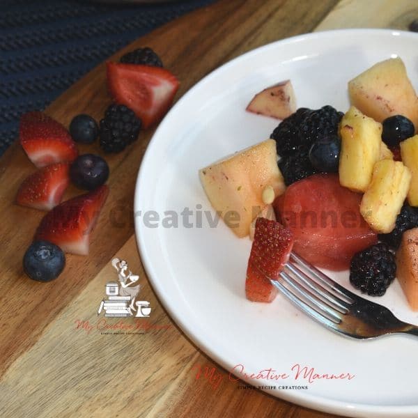 Fruit on a white plate with a fork that has a strawberry on it.