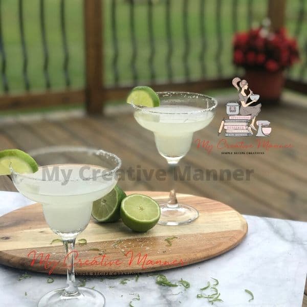 Two Margarita cocktails on a table with limes.