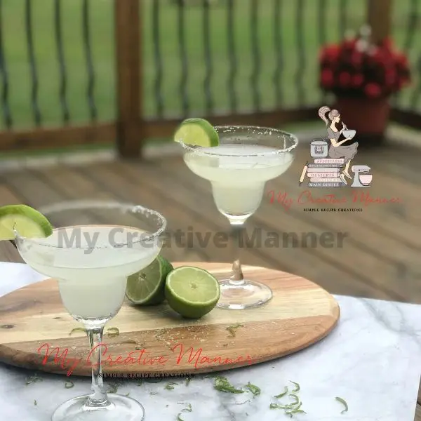 Two Margarita cocktails on a table with limes.