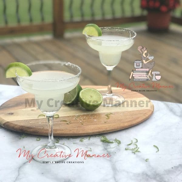 Two glasses filled with the cocktail recipe in it on a board with limes.
