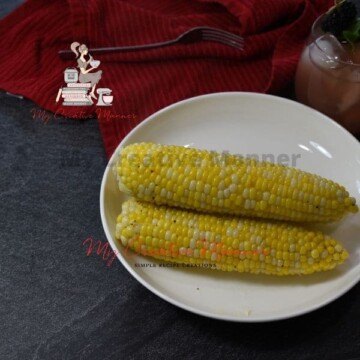 Three fresh corn on the cob that are on a white plate.
