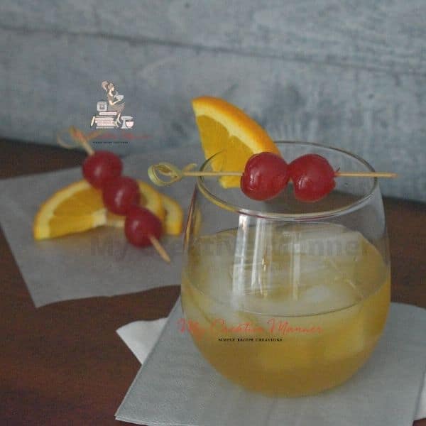 Whiskey drink with a cherry and orange garnish.