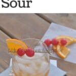 Whiskey sour cocktail recipe on a napkin with a toothpick that has cherries and orange slice.