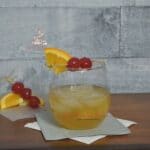 A whiskey sour drink on a table with a toothpick that has two cherries on it.