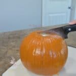 A pie pumpkin being cut with a knife.