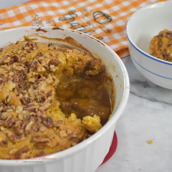 Pumpkin pecan cobbler in a baking dish with a small bowl that has some in it.