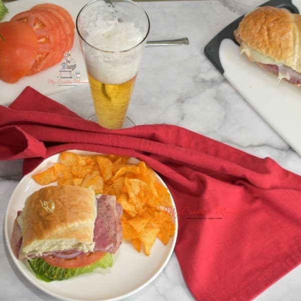 A sandwich on a plate with chips and a beer.