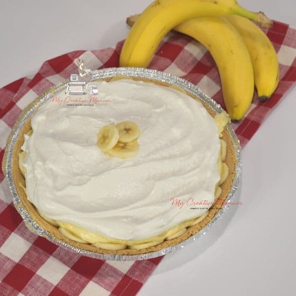 A completed cream pie with bananas next to it.