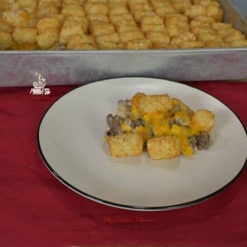 Tater Tot casserole on a white plate with more of the casserole recipe in the baking dish.