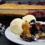 A close up of the blueberry dump cake dessert recipe that is on a plate with the rest of the dessert in the baking dish.