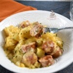 Crockpot potatoes and sausage in a white bowl with a fork in the food.