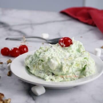 Pistachio fluff piled in a white dish with a cherry on top.