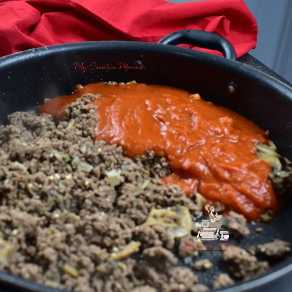 Ground beef with pasta sauce in a frying pan.