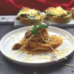 A simple pasta recipe on a plate with cheese toast in on a platter behind the plate.