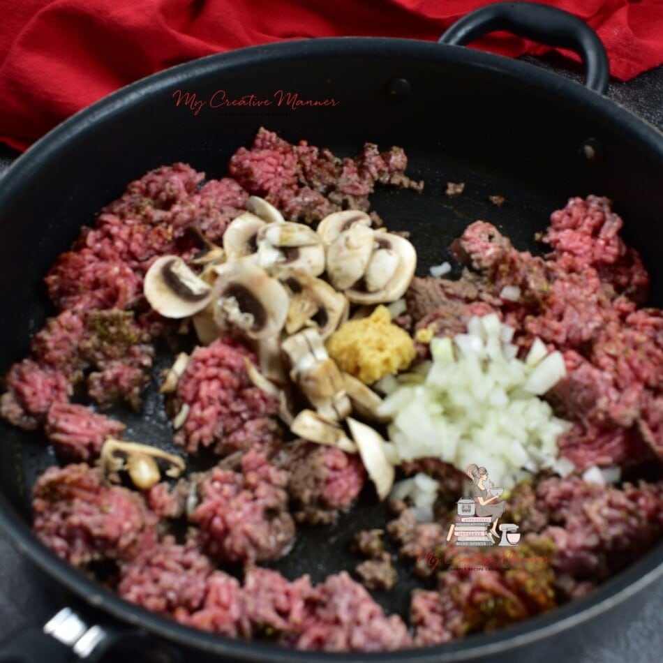 Ground beef that has garlic, onion, and mushrooms in a frying pan.