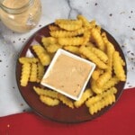 Srirach Fry Sauce in a bowl with fries around it on a plate.