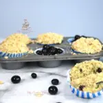 Banana blueberry muffins in a muffin tin and a muffin that is in front of the tin.