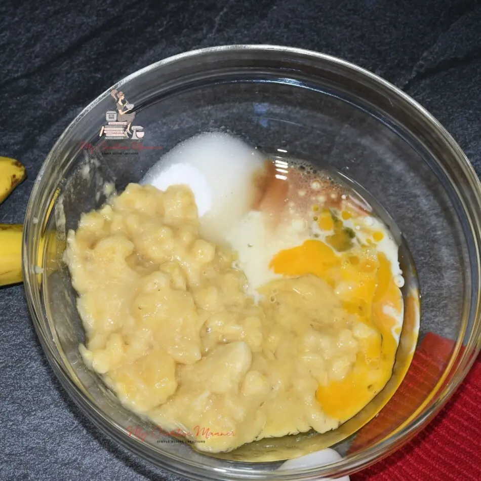 Mashed bananas, sugar, eggs, milk, and oil in a mixing bowl.