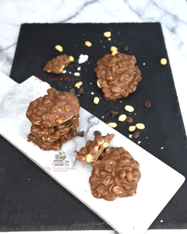 Crock Pot Peanut clusters on a white marble plate with more on a black tray.