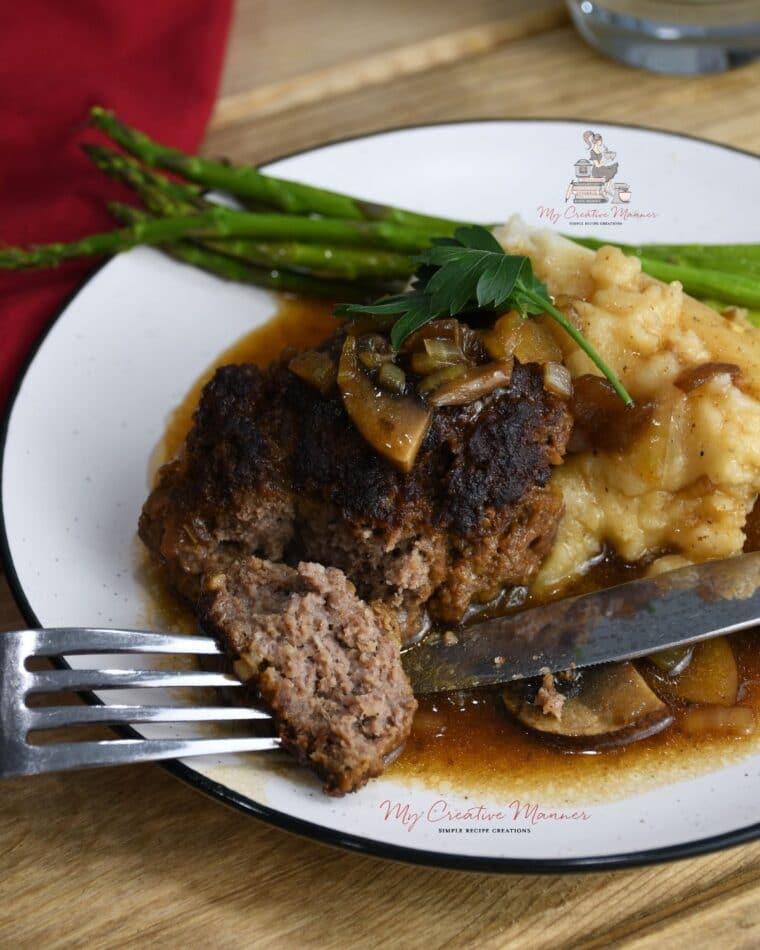 Hamburger steak with gravy on a plate with mashed potatoes and asparagus.