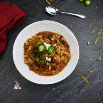 Instant Pot Chili Mac in a white bowl with a spoon and red napkin on the sides of the bowl.