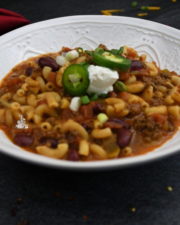 A bowl of chili mac with sour cream and jalapeno on top of it.