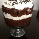 A trifle dish that has layers of chocolate cake, chocolate pudding, whipped topping, and is sprinkled with mini chocolate chips.