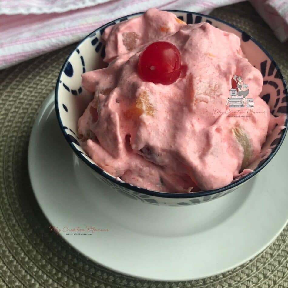 Strawberry jello fluff salad in a bowl with a spoon next to it.