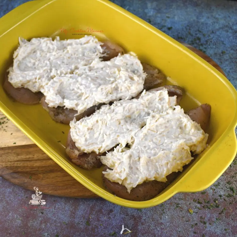 Raw chicken breast with a creamy parmesan mayo dressing on it.