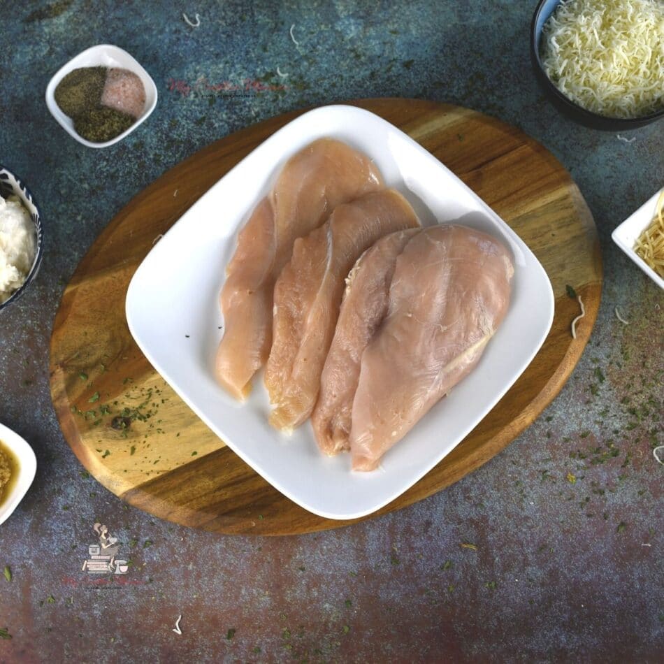 Raw chicken breast for parmesan mayo chicken on a white plate.