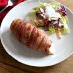 A bacon wrapped chicken breast with salad on a plate.