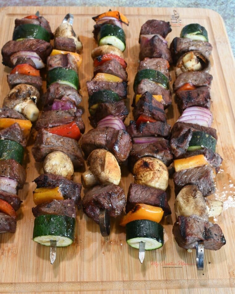 Four grill kabobs on a wood cutting board.