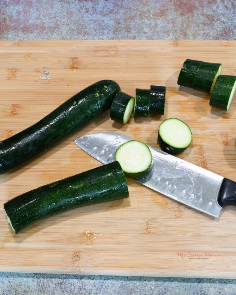 Zucchini that is on a cutting board that is being sliced.