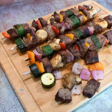 Kabobs on a cutting board with some of the kabobs loosely on the board.