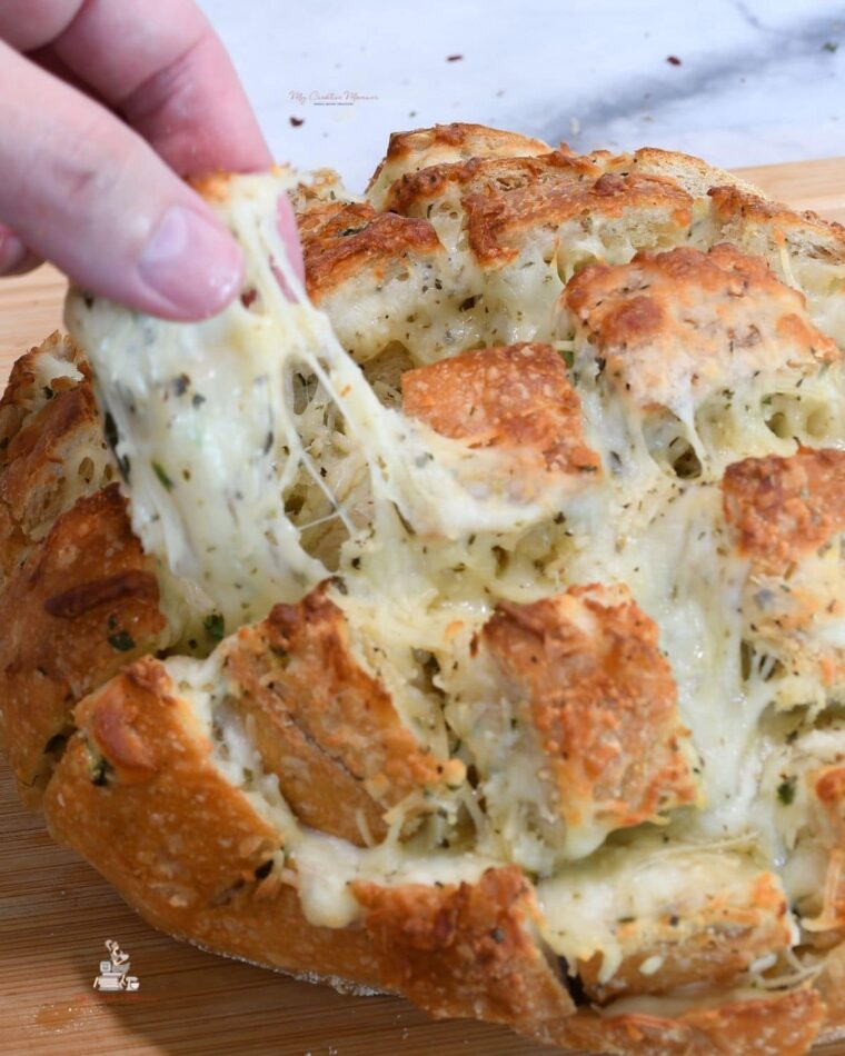 Fingers pulling a piece from the cheesy pull apart garlic crack bread.