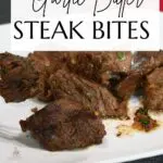 A plate full of steak bites that are in a garlic butter sauce.