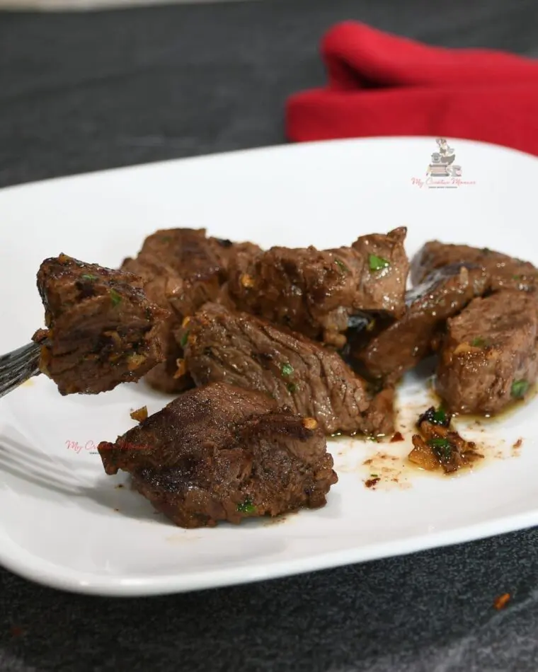 Sirloin tips on a white plate that have been coated in a butter sauce.