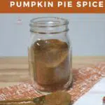 A mini mason jar with the homemade pumpkin pie spice in it. Along with a measuring spoon that has some in it.