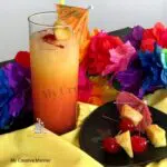 A glass that is filled with a bahama mama cocktail that is made with Malibu rum. With a plate of pineapple and cherries next to it.