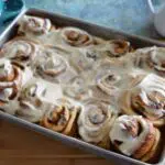 A sheet pan filled with baked cinnamon roll buns that are topped with cream cheese icing.