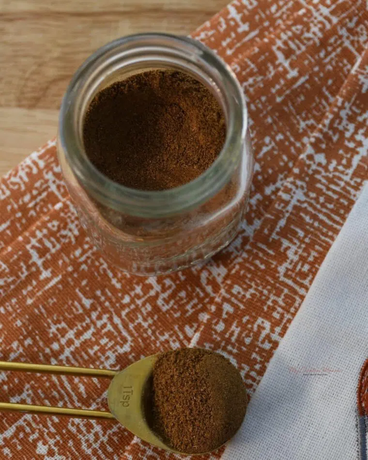A mini mason jar that has all the ingredients for pumpkin pie spice in it. With a measuring spoon filled with the spice next to it.